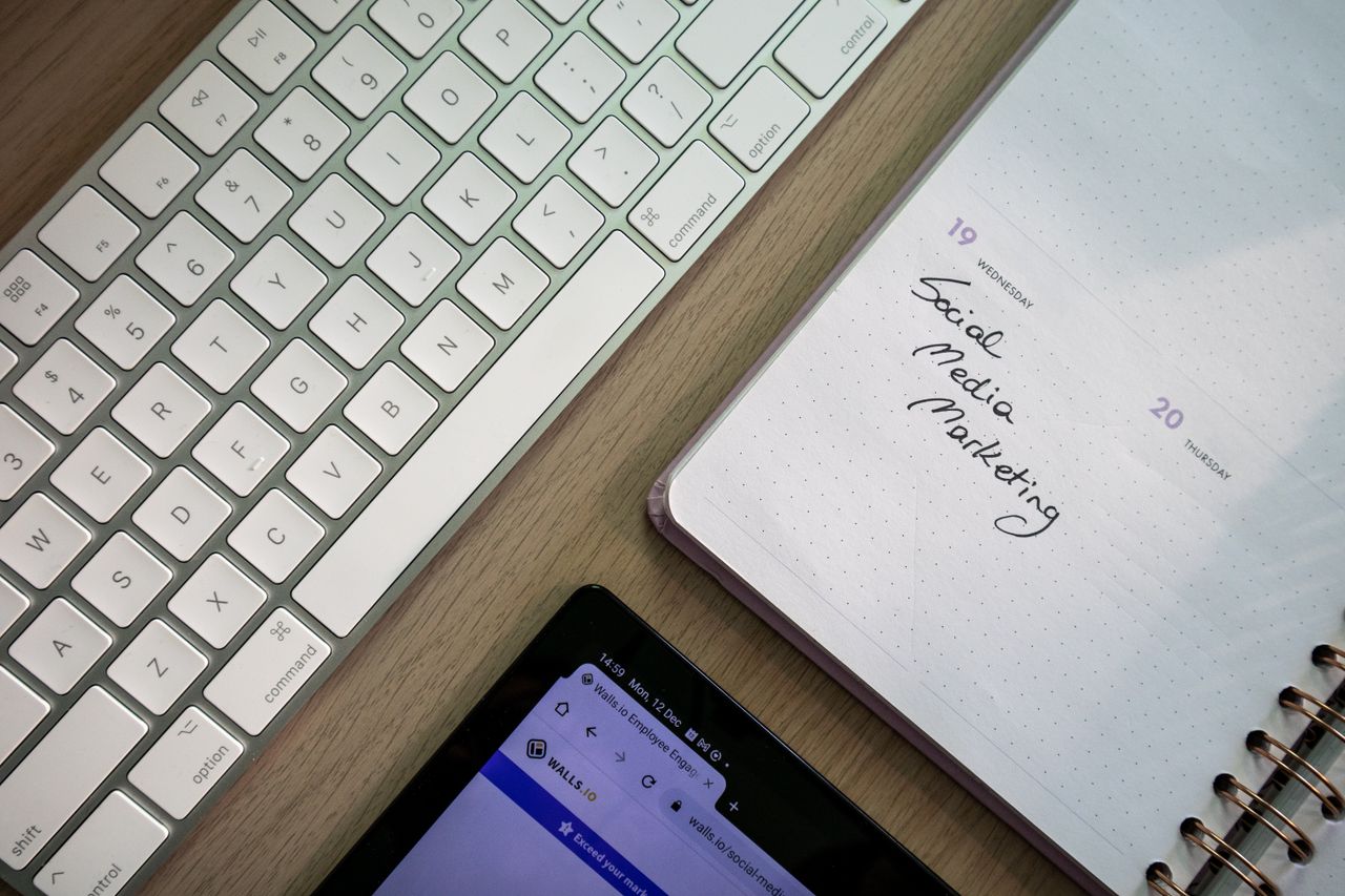 Top view of keyboard, planner with social media marketing note, and tablet on a desk.